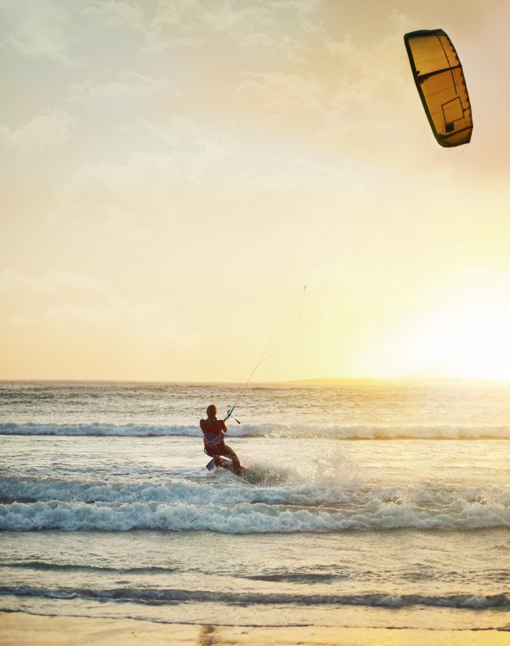 Shes at one with the wind and waves. Rearview shot of a young woman kitesurfing at the beach